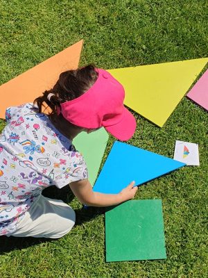fetita joaca tangram colorat gigant pe iarba verde