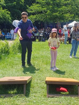 Tată și fiică joacă Cornhole pe iarbă, aruncând săculeți colorați spre platforme cu gaură