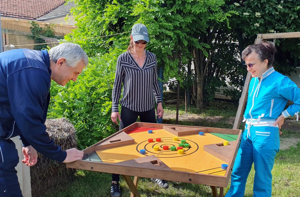 Reconectare prin joaca când un bărbat mai în vârstă, două femei adulte, în interacțiune relaxată și prietenoasă joacă un joc din lemn, colorat, zâmbesc și sunt atenți, transmit bucurie autentică