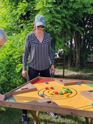 Reconectare prin joaca când un bărbat mai în vârstă, două femei adulte, în interacțiune relaxată și prietenoasă joacă un joc din lemn, colorat, zâmbesc și sunt atenți, transmit bucurie autentică