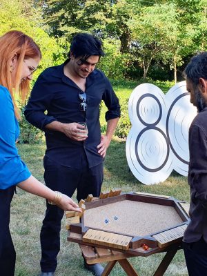 Adulți jucând Shut the Box la eveniment în aer liber, joc de strategie și matematică din lemn pentru teambuilding