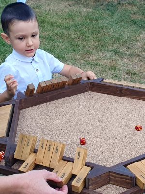 Copil de vârstă mică jucând Shut the Box uriaș din lemn în timp ce învață matematică, ghidat de animator profesionist