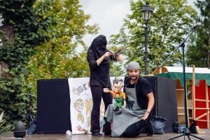 Doi artiști mânuind marioneta Pinocchio pe scenă în aer liber la festival în Brașov