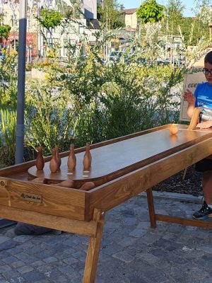 Copil lansează bila cu brațul de lemn la jocul Zece Popice, mini bowling din lemn masiv, la un eveniment în aer liber